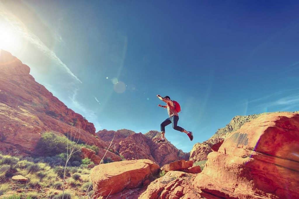 Man jumping from a boulder in a desert for our outback camping tips article