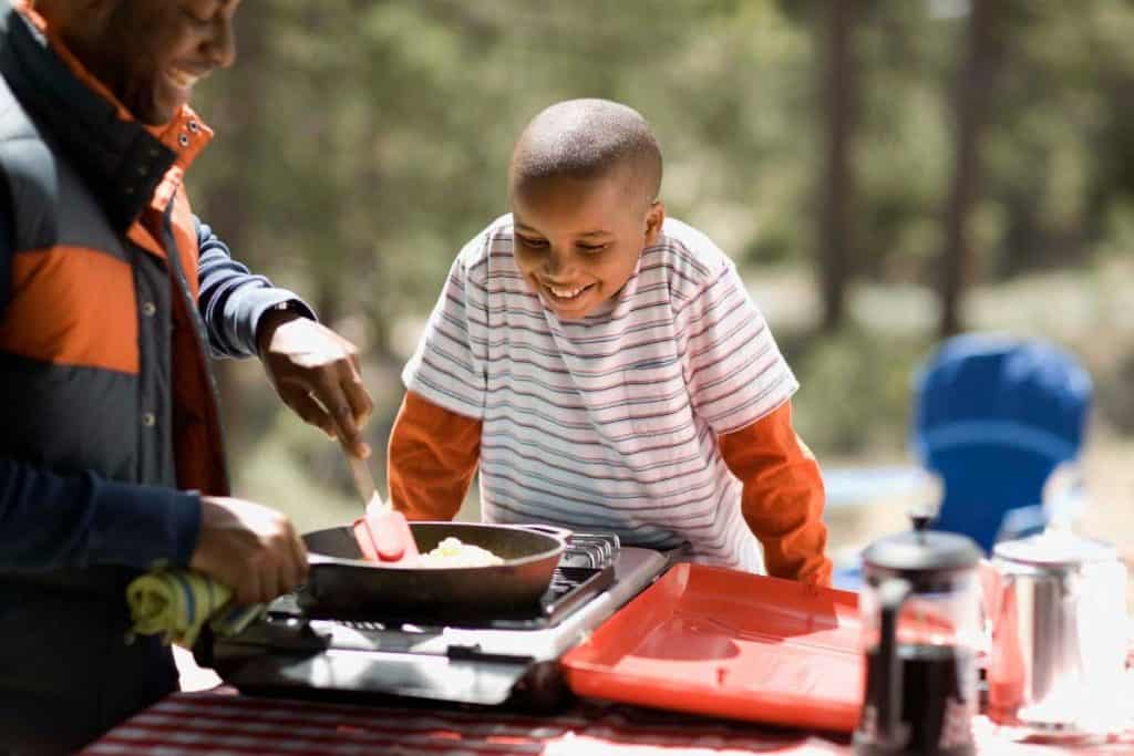 Son watches father cook food in camp
